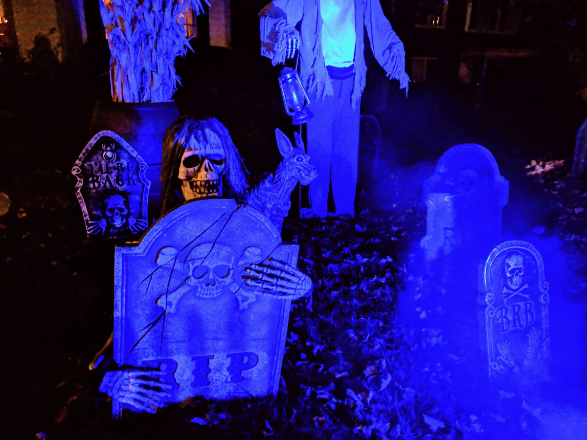 Tombstones in the cemetery, a skeleton peering over the RIP stone, lit blue